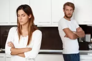 Eine Frau mit verschränkten Armen und ein Mann im Hintergrund. Glaubenssätze verhindern die Heilung des Inneren Kindes.