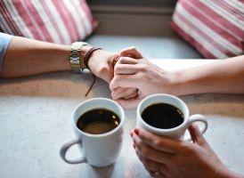 Ein Paar hält sich an den Händen, bei einer Tasse Kaffee. Rituale helfen, die Liebe im Alltag zu bewahren.
